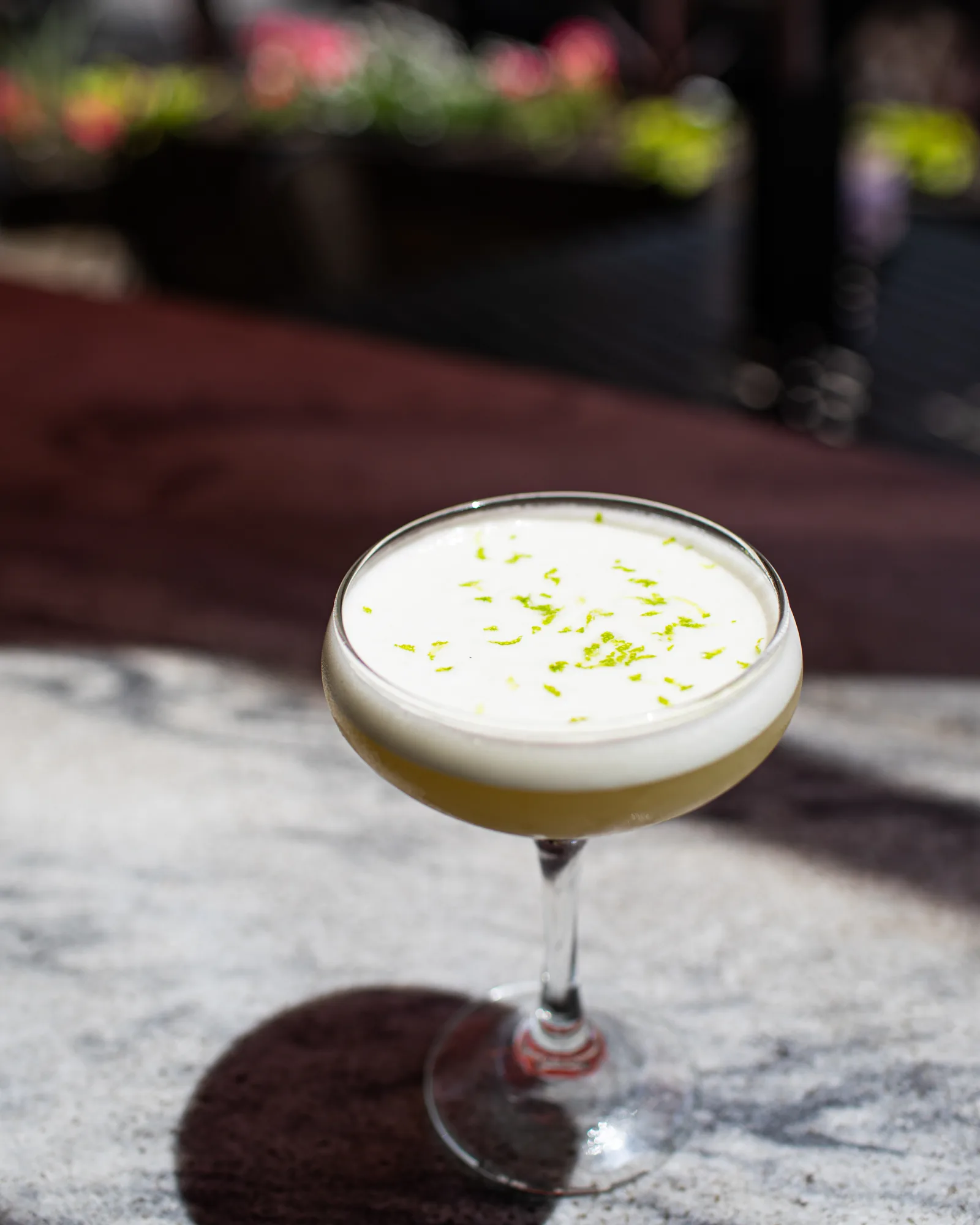 A frothy lime sour cocktail in a coupe, in the sun